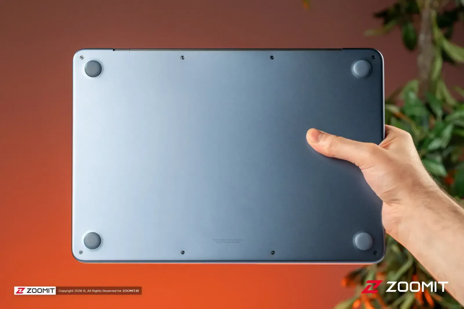 بدنه زیرین لپتاپ مک بوک نئو (MacBook Neo) در دست یک فرد
