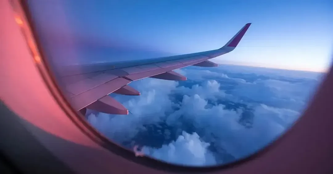 بال هواپیما در حال پرواز بر فراز ابرها در هنگام غروب