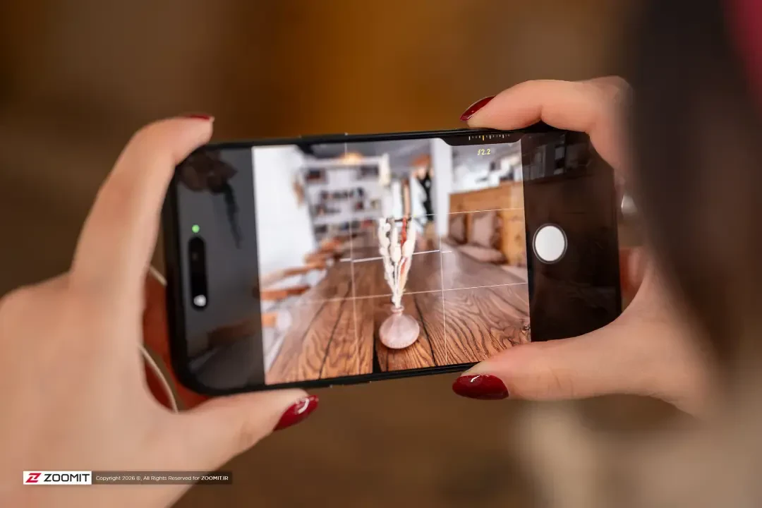 آیفون ۱۸ پرو مکس (iPhone 18 Pro Max) در حال عکاسی از یک میز چوبی