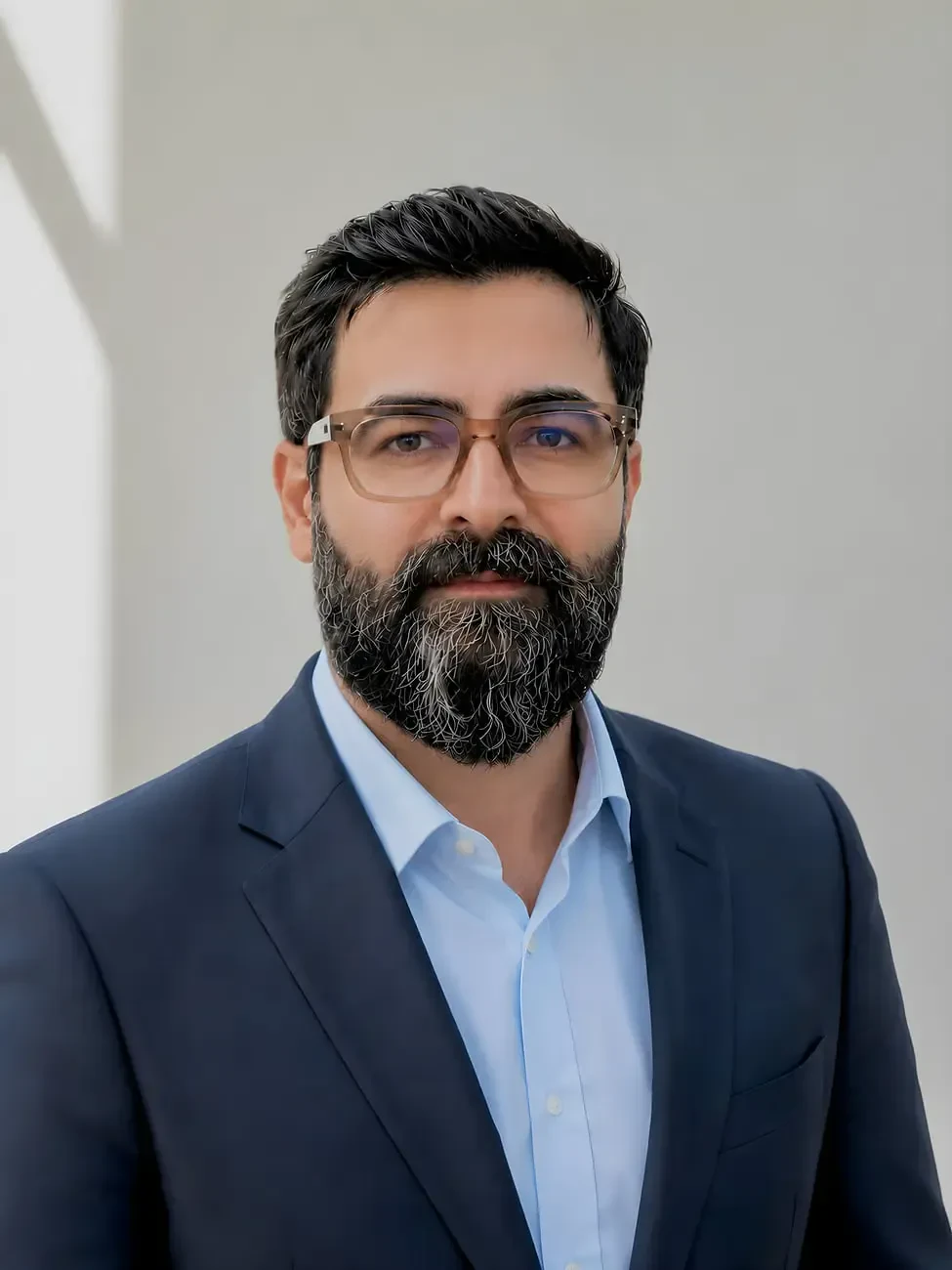 مردی با عینک و ریش که در پسزمینهای روشن ایستاده است